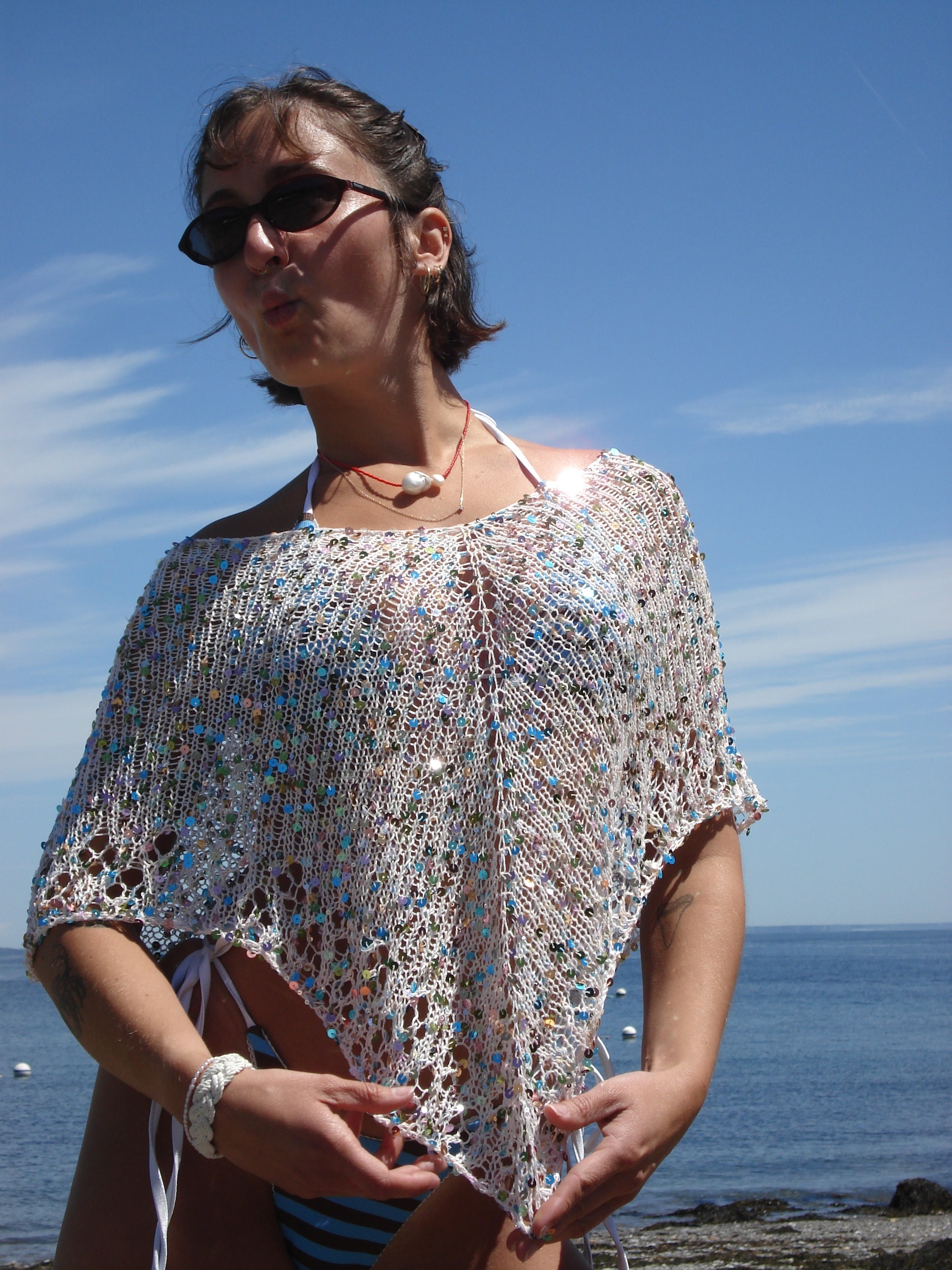 Woman wearing a sparkly knit poncho by the ocean
